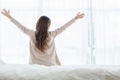 Back view of happy beautiful young Asian woman waking up in morning, sitting on bed, stretching in cozy bedroom. Royalty Free Stock Photo