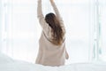 Back view of happy beautiful young Asian woman waking up in morning, sitting on bed, stretching in cozy bedroom. Royalty Free Stock Photo