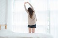 Back view of happy beautiful young Asian woman waking up in morning, sitting on bed, stretching in cozy bedroom. Royalty Free Stock Photo