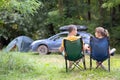 Back view of a happy couple sitting on chairs at campsite relaxing together. Travel, camping and vacations concept
