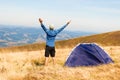 Happy traveler man on top of mountain raised hands enjoying freedom and view near tent camping outdoor. Travel adventure lifestyle Royalty Free Stock Photo