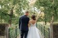 Happy wedding couple embracing on bridge near trees in park in summer. Young woman bride preparing to throw bouquet. Royalty Free Stock Photo
