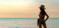 Back view of happy young Asian woman in black swimsuit and straw hat relax and enjoy holiday at tropical paradise beach at sunset. Royalty Free Stock Photo