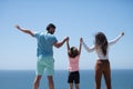 Back view of happy young family walking on beach. Child with parents holding hands. Full length poeple. Royalty Free Stock Photo