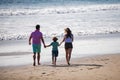 Back view of happy young family walking on beach. Child with parents holding hands. Full length poeple. Royalty Free Stock Photo