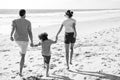 Back view of happy young family walking on sand beach. Child with parents holding hands. Full length poeple. Royalty Free Stock Photo