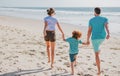 Back view of happy young family walking on sand beach. Child with parents holding hands. Full length poeple. Royalty Free Stock Photo