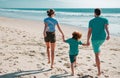 Back view of happy young family walking on sand beach. Child with parents holding hands. Full length poeple. Royalty Free Stock Photo