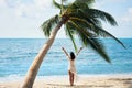 Back view of happy young woman enjoy her tropical beach vacation standing under palm tree Royalty Free Stock Photo