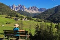 Back view of a hiker sitting on a wooden bench at the idyllic St. Magdalena, Dolomites, Itay