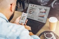 Back view. Hipster man sits in cafe, uses smartphone, works on laptop with graphs, charts, diagrams on monitor Royalty Free Stock Photo