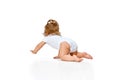 Back view image of little, baby girl in diaper crawling on floor, playing against white studio background. Royalty Free Stock Photo