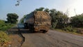 Back view of Indian trucks passing on the road early in the morning, road covered by green trees.