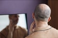 Back view of insecure bald man looking in mirror