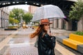 Back view of joyful redhead young woman walking on beautiful city street with transparent umbrella enjoying rainy Royalty Free Stock Photo