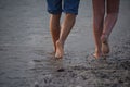 Back view of the legs of a couple walking barefoot on a muddy beach