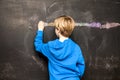 Back view of a little boy painting something on a chalkboard