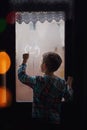 Back view of little child drawning smile on fogged glass looking through the window Royalty Free Stock Photo