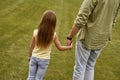 Back view of a little girl holding hand of her father while spending time together outdoors