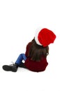 Back view of little girl in red Santa hat sitting on the floor looking up. Rear view. Royalty Free Stock Photo