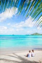 Back view of little girls on sandy beach. Happy kids sitting under the palm tree on tropical beach Royalty Free Stock Photo