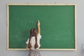 Back view of little student girl writing down arithmetic sum green school chalkboard Royalty Free Stock Photo