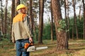 Back view of logger wearing protective helmet and uniform holding chainsaw in hands, looking around before starting deforestation