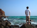 Back view of lonely Asian man standing on the stone of sea shore and looking at far away. Royalty Free Stock Photo