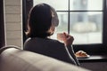 Back view of lonely ÃÂaucasian young woman enjoying having breakfast with cup of hot chocolate and croissant, listenning music