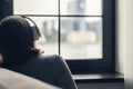 Back view of lonely brunette woman in headphones listen music sitting near window . Concept. Royalty Free Stock Photo