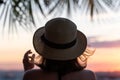 Back view of a lonely girl in a straw hat against the background of the sea in branches of palm trees. Sunset beach. Woman waving Royalty Free Stock Photo
