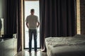 Back view of lonely isolation middle-aged gray-haired man standing near open window of apartment or hotel room. Royalty Free Stock Photo