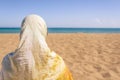 Back view of lonely Muslim woman  traveler in a colorful headscarf, scarf on the sand on the beach and looking on the sea. Royalty Free Stock Photo