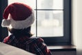 Back view of lonely sad young woman in a red santa claus christmas hat sitting and looking at window. Royalty Free Stock Photo