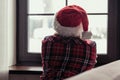 Back view of lonely sad young woman in a red santa claus christmas hat sitting and looking at window. Royalty Free Stock Photo