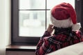 Back view of lonely sad young woman in a red santa claus christmas hat sitting and looking at window. Royalty Free Stock Photo