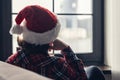 Back view of lonely sad young woman in a red santa claus christmas hat sitting and looking at window. Royalty Free Stock Photo