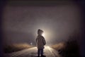 Back view of lost child was standing in the middle of a street lit by the headlights of cars in the dark background. People and Royalty Free Stock Photo