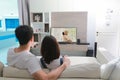 Back view of lovers hugging and sitting on sofa and watching TV in living room