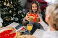 Back view of loving grandmother giving festive box with Christmas present to adorable granddaughter sitting at dinner Royalty Free Stock Photo