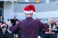 Back view of a male conductor, wearing casual outfit with red santa hat, conducting his young band performing Christmas music at