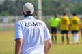 Back view of male football coach in white COACH shirt at an outdoor sport field