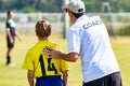 Back view of male football coach in white COACH shirt at an outdoor sport field sending his young boy player in the game