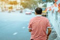 Back view of male patient with mask in red and white shirt standing at bus stop and wait for taxi or bus in the city to go to the Royalty Free Stock Photo
