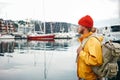 Back view of male tourist with traveling rucksack standing among fishing boat on city pier Royalty Free Stock Photo