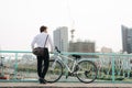 Back view man with a bicycle stands on the bridge looking at the city