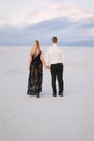 Back view of man and blonde girl wearing black dress walking in snowed steppe. Royalty Free Stock Photo