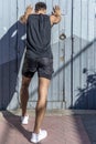 Rear view of a man doing stretching leaning on a wooden door on a summer morning