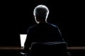 Back view of a man with gray hair working from home late at night using his laptop computer Royalty Free Stock Photo