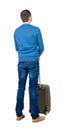 Back view of man with green suitcase looking up.